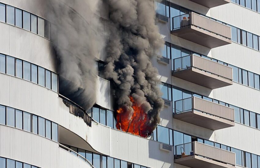 Incêndio em prédio alto com fumaça e fogo visíveis na janela.