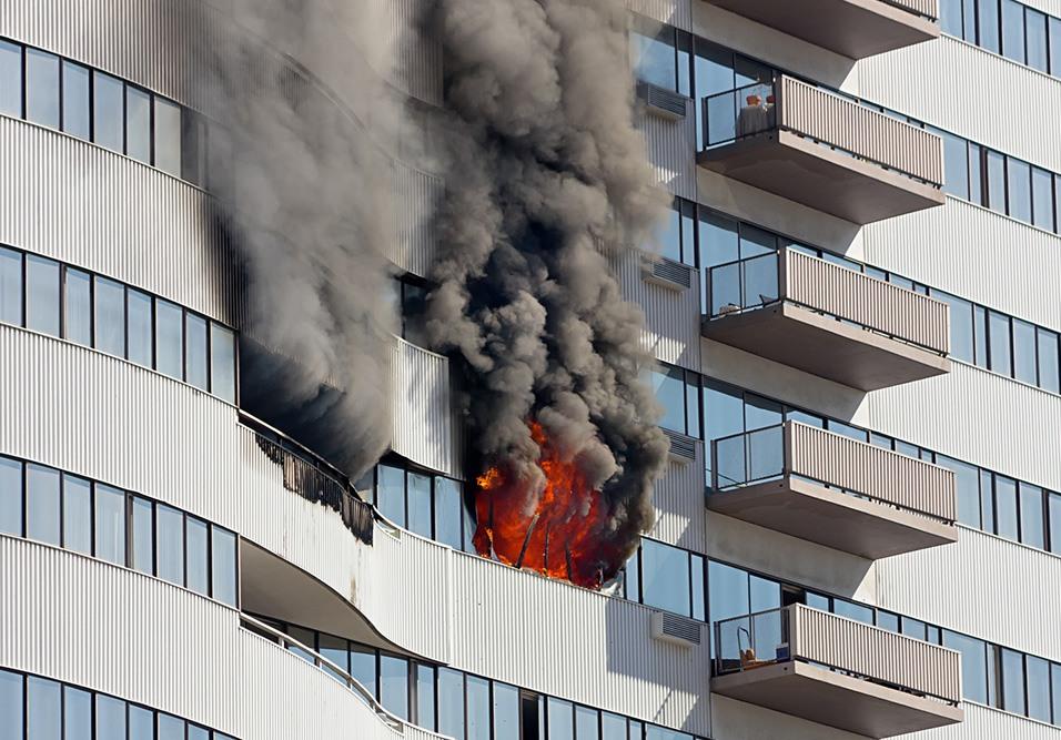 Incêndio em prédio alto com fumaça e fogo visíveis na janela.