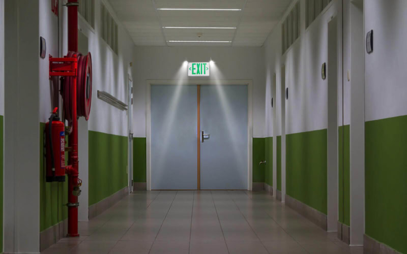 Sinalização de saída de emergência com iluminação de emergência em corredor de edifício.