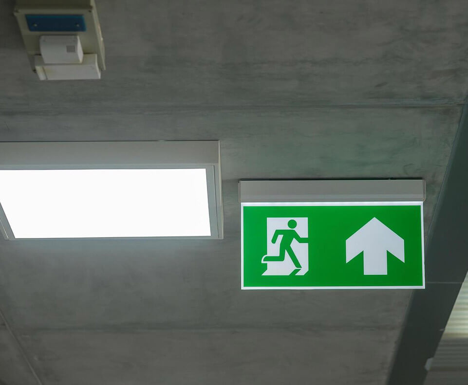 Sinal de saída de emergência com iluminação verde e símbolo de pessoa saindo.